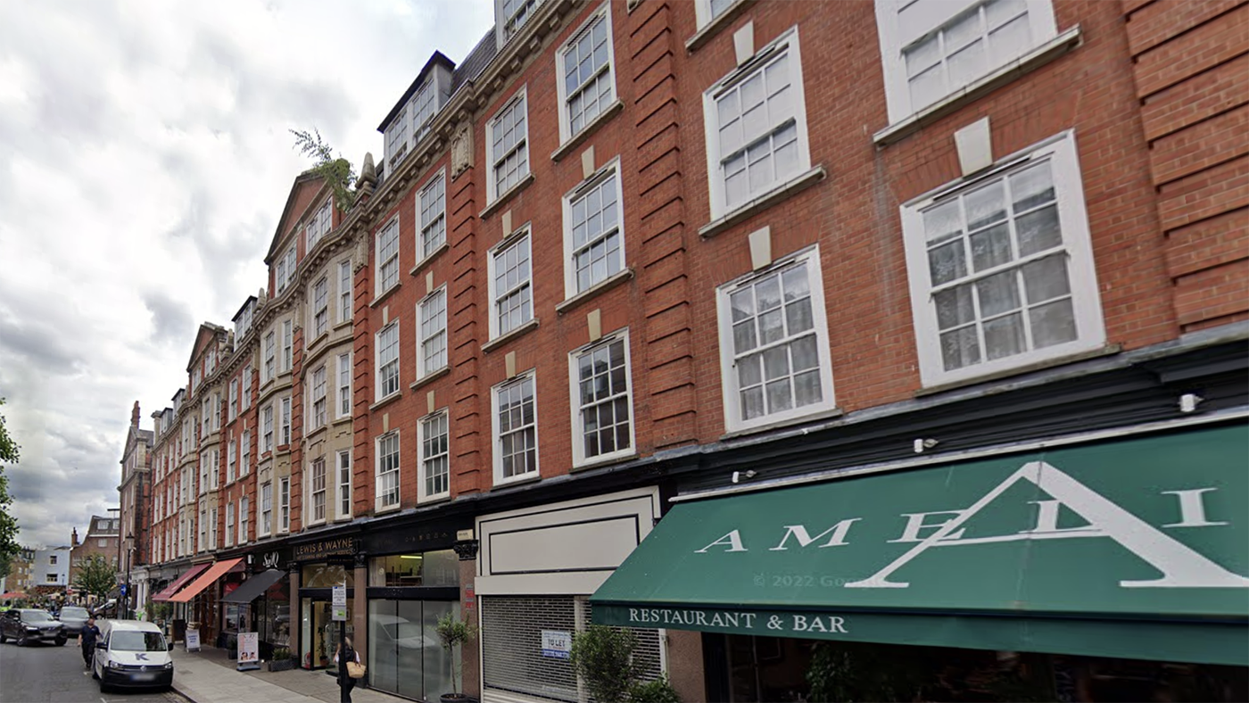 A row of red-brick buildings with ground-floor shops and a restaurant on a city street.